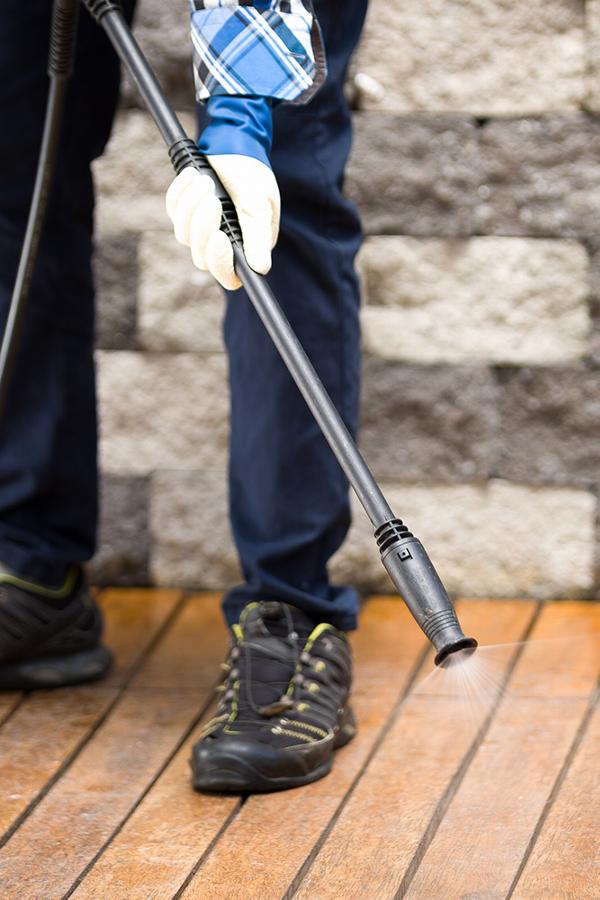 Close up of gardener spraying wooden deck with pressure washer